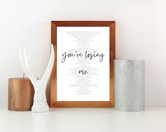 May include: A framed print with the words "you're losing me" in a handwritten font. The print is in a gold frame, and the background is white. A white decorative antler and two candles, one copper and one silver, are next to the frame.