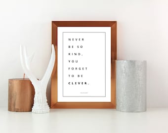 May include: A copper-coloured framed print with the quote "Never be so kind, you forget to be clever." The print is sitting on a white surface with a white antler figurine and two candles, one copper and one silver.
