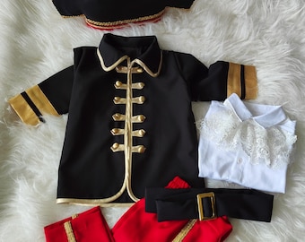 May include: A pirate costume set featuring a black hat with a skull and crossbones, a black jacket with gold trim and buttons, red pants with gold stripes, a white shirt, and a black belt with a gold buckle.