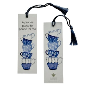 May include: Two rectangular paper bookmarks with dark blue tassels. Each features a vertical stack of four blue and white teacups. The left bookmark displays the text A proper place to pause for tea. The right bookmark features the Forever Caroline logo.