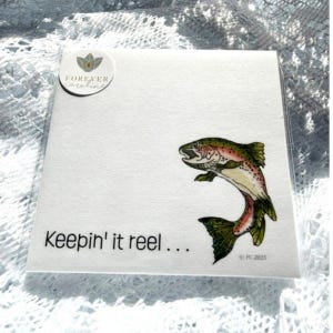 May include: A square white card featuring a colorful illustration of a jumping trout. The text "Keepin' it reel..." is printed in black on the lower left. A circular logo with the text "FOREVER caroline" is in the top left corner.