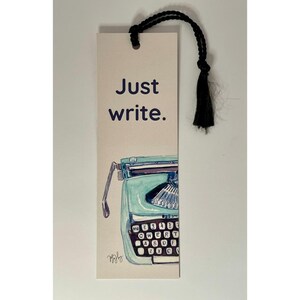 May include: Bookmark with a teal typewriter illustration and the words "Just write." A black tassel hangs from the top. The typewriter has a keyboard with the letters QWERTY.