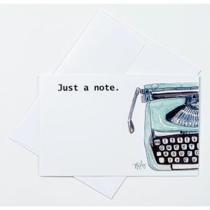May include: A white greeting card with the text "Just a note." features a watercolor illustration of a vintage teal typewriter. The card is accompanied by a white envelope, perfect for sending a personalized message.