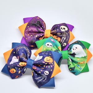 May include: Three hair bows made of grosgrain ribbon featuring Halloween patterns. The bows display prints of skeletons, ghosts, pumpkins, black cats, and sweets in purple, orange, green, and blue colours with a central knotted ribbon band.