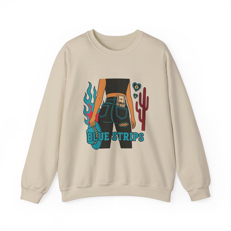 May include: A beige sweatshirt with a graphic print of a woman wearing blue jeans with a dollar bill in the back pocket. The graphic also includes a cactus, flames, and a cowboy hat. The text "BLUE STRIPS" is printed below the graphic.