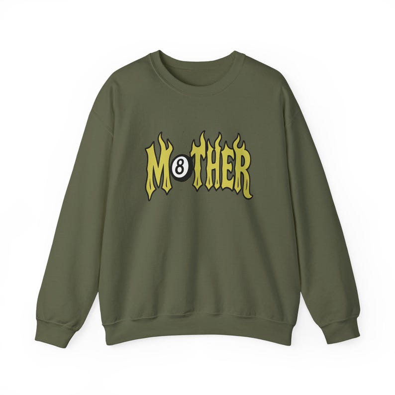 K&ouml;nnte beinhalten: Olivgr&uuml;nes Sweatshirt mit dem Wort "MOTHER" in gelben, flammenartigen Buchstaben. Der Buchstabe "O" ist durch eine 8-Ball-Grafik ersetzt. Das Sweatshirt hat einen Rundhalsausschnitt und lange &Auml;rmel.