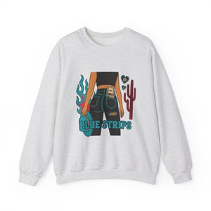 May include: A grey sweatshirt with a graphic print of a woman in blue jeans with a bill tucked in the back pocket. The graphic also includes a cactus, flames, and the text "BLUE STRIPS".