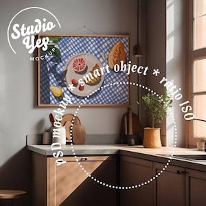 Könnte beinhalten: Ein gerahmter Druck eines Stilllebens mit einem Teller Obst auf einer blau-weiß karierten Tischdecke. Das Bild hängt an einer Wand in einer Küche mit Holzschränken und einem Spülbecken.