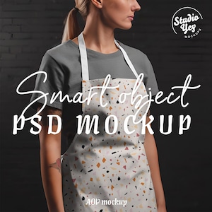 Könnte beinhalten: Eine Frau trägt ein graues T-Shirt und eine weiße Schürze mit einem Terrazzo-Muster. Die Schürze hat den Text "AOP mockup" unten aufgedruckt. Der Text "Smart object PSD MOCKUP" ist in Weiß auf schwarzem Hintergrund geschrieben.