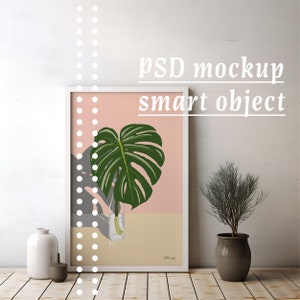 Könnte beinhalten: Ein weißer gerahmter Poster mit rosa Hintergrund und einer grünen Monstera-Pflanze in einer durchsichtigen Glasvase. Der Poster hängt an einer weißen Wand mit einer kleinen Topfpflanze in der Ecke.