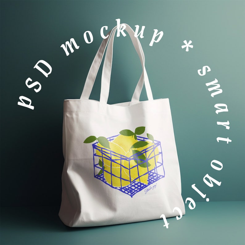 May include: White canvas tote bag with a blue and yellow illustration of lemons in a wire basket. The text "PSD mockup * smart object" is written in white around the bag.