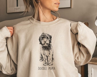 May include: A beige sweatshirt with a black and white illustration of a doodle dog wearing a bandana. The text "Doodle Mama" is printed below the dog.