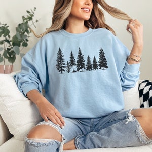 May include: A light blue sweatshirt with a black silhouette of a row of pine trees printed on the front.