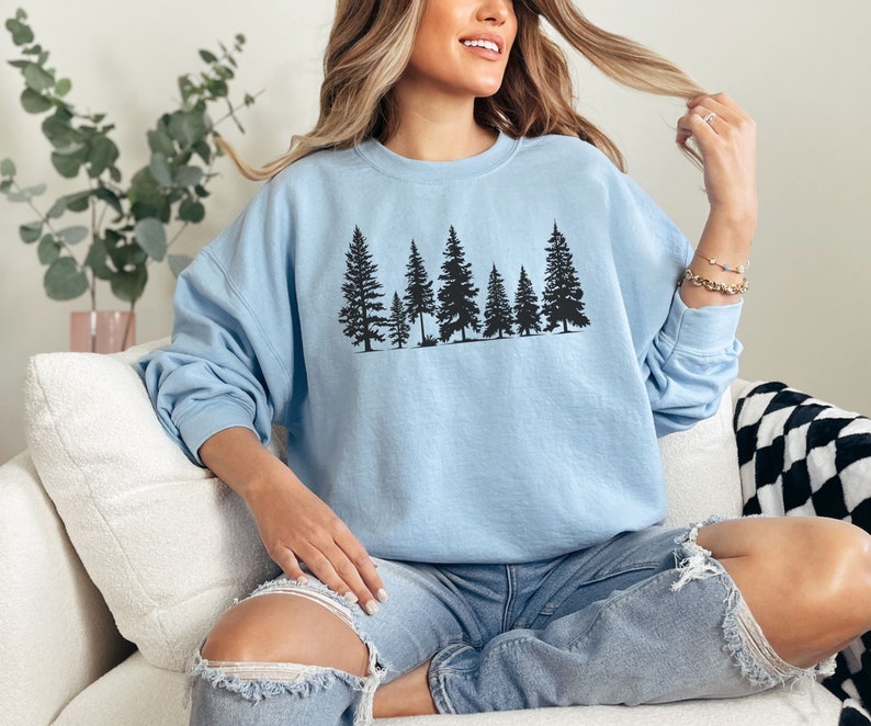 May include: A light blue sweatshirt with a black silhouette of a row of pine trees printed on the front.