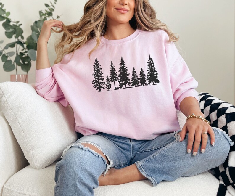 May include: A pink sweatshirt with a black silhouette of a row of pine trees printed on the front.