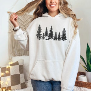 May include: White hooded sweatshirt with a black silhouette of a row of pine trees printed on the front.