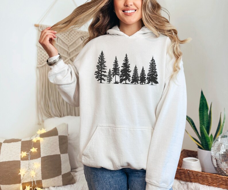 May include: White hooded sweatshirt with a black silhouette of a row of pine trees printed on the front.