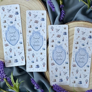 May include: Four rectangular bookmarks with a light blue and white design, featuring illustrations of keys, teacups, and books. Each bookmark has the text "Dearest Gentle Reader" in a blue frame. The bookmarks are arranged on wooden slices, with lavender sprigs.