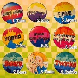 Op de afbeelding: Een verzameling van negen kleurrijke ronde buttons. Elke button bevat tekst en ontwerpen, waaronder zinnen als "Trans", "Enby", "Aroace", "Pan", "Bi", "Lesb", "Bears", "Tintin" en "Twinks". De buttons hebben verschillende kleurenschema's.