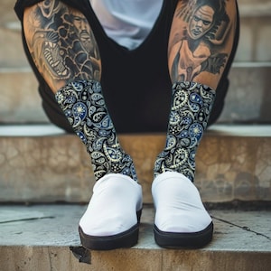 Pode incluir: Um par de meias brancas com um padrão paisley preto e azul. As meias são usadas por uma pessoa com tatuagens nas pernas.