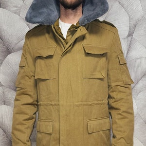 Op de afbeelding: Een bruin jack in militaire stijl met een grijze bontkraag. Het jack heeft meerdere zakken en een knoopsluiting.