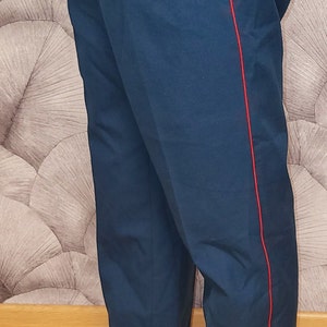 Peut inclure: Pantalon bleu foncé avec une bande rouge sur la couture latérale. Le pantalon est fait d'un tissu épais et résistant et a une coupe classique et ajustée.
