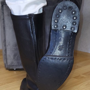 May include: Black leather riding boots with a zipper on the back and a thick rubber sole. The sole has a pattern of small circles and the text "44 6F" is visible on the sole.