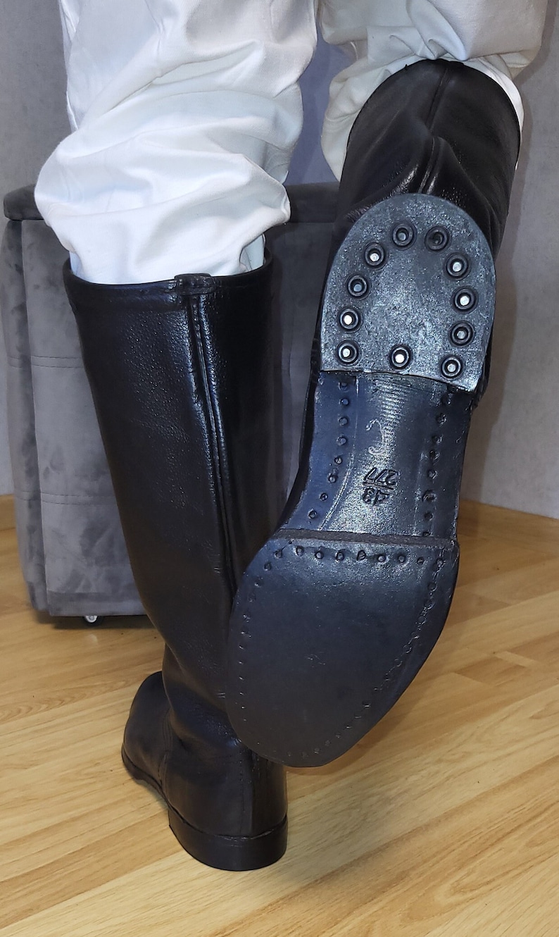 May include: Black leather riding boots with a zipper on the back and a thick rubber sole. The sole has a pattern of small circles and the text "44 6F" is visible on the sole.