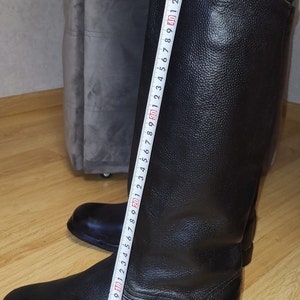 May include: Black leather riding boots with a zipper on the back. The boots are measured with a tape measure, showing a length of 40 cm.