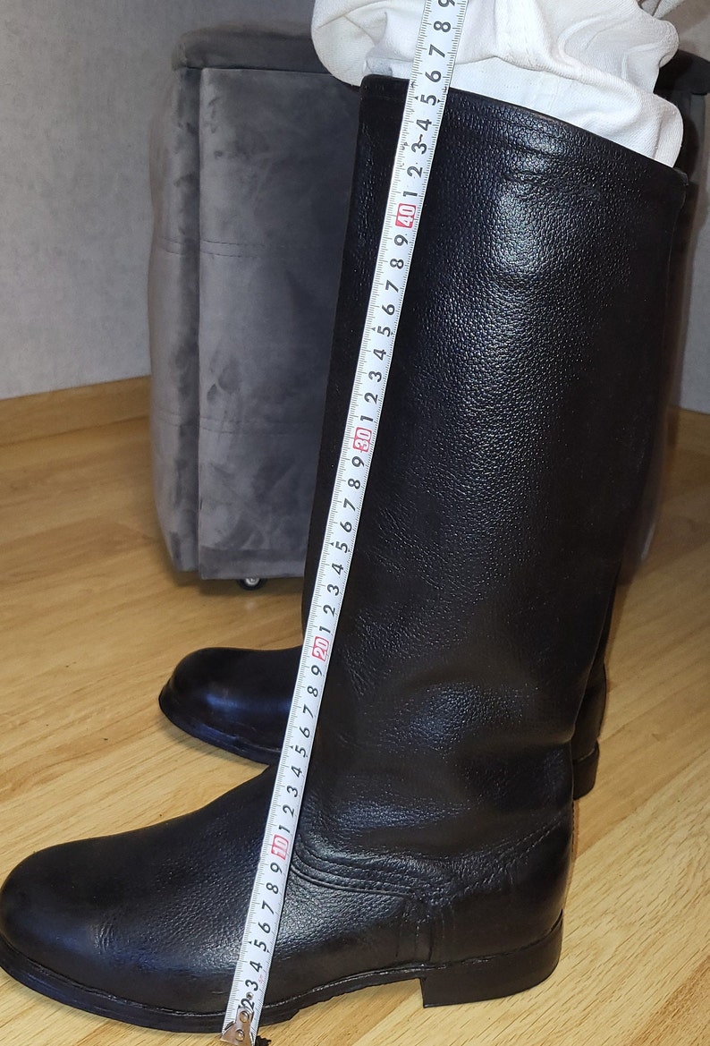 May include: Black leather riding boots with a zipper on the back. The boots are measured with a tape measure, showing a length of 40 cm.