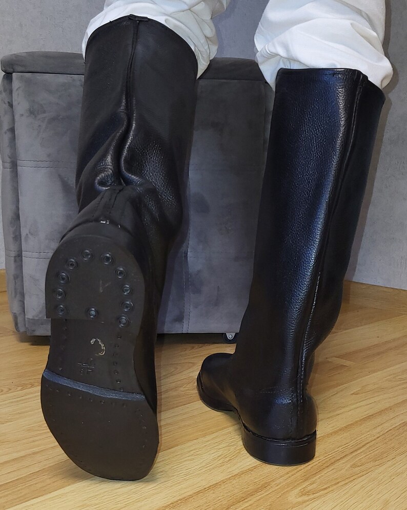 May include: A pair of black leather knee-high boots with a pointed toe and a low heel. The boots are made of a smooth leather and have a zipper on the back.