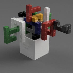 May include: A colourful abstract sculpture made of small, interlocking blocks. The sculpture is composed of red, green, white, black, blue, and yellow blocks. The sculpture is sitting on a white cube with the text "PROTOTYPE 007/252" printed on it.