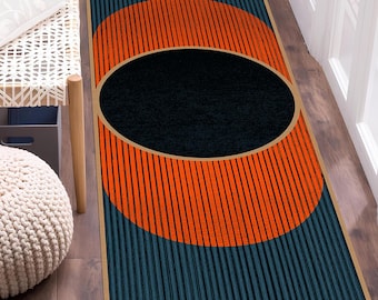 Puede incluir: Una alfombra de pasillo rectangular con fondo azul oscuro y rayas verticales. El centro muestra un gran círculo naranja intenso que contiene una forma ovalada negra sólida. El diseño está enmarcado por un borde fino de color claro.