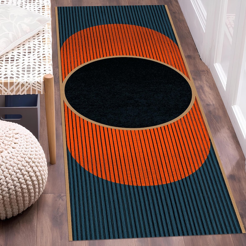 May include: A rectangular rug with a geometric design. The rug features a large orange circle with black vertical lines, a black oval in the center, and teal vertical stripes. The rug is bordered with a tan trim.