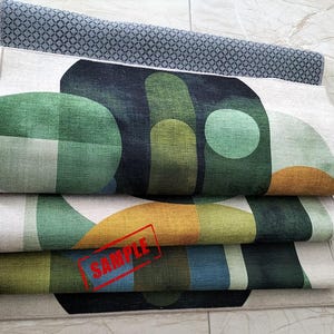 May include: Folded rugs with geometric designs in shades of green, blue, and gold. The top rug has a gray diamond pattern. The rugs are stacked, showcasing the colorful patterns and textures. The word "SAMPLE" is stamped on one of the rugs.