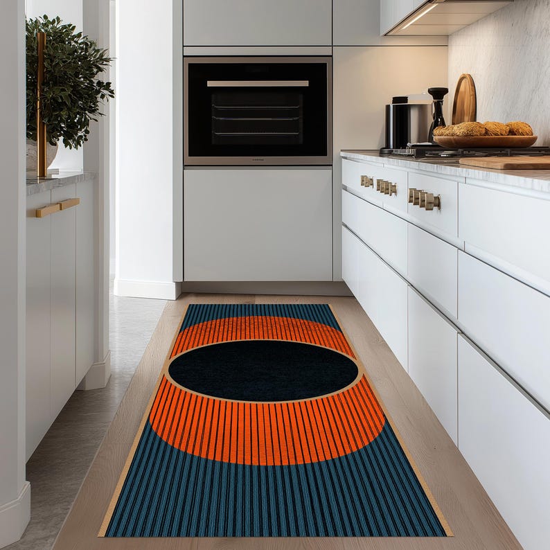 May include: A rectangular kitchen rug with a geometric design. The rug features a large orange semi-circle with vertical black lines, a black oval, and blue vertical lines. The rug is placed on a light wood floor.