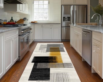Puede incluir: Una alfombra rectangular con un patrón geométrico abstracto de bloques superpuestos en negro, gris carbón y amarillo mostaza sobre un fondo color crema. El diseño incluye detalles lineales texturizados y formas rectangulares sólidas.