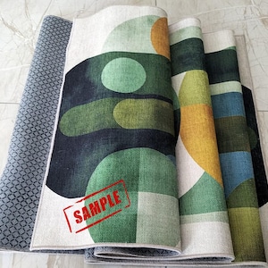 May include: Rolled-up area rugs with geometric designs in shades of green, yellow, blue, and white. The rugs have a textured appearance and a gray patterned backing. A red "SAMPLE" stamp is visible on one rug.