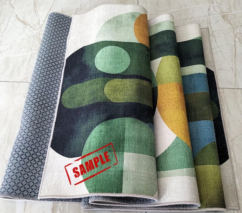 May include: Rolled-up area rugs with geometric designs in shades of green, yellow, blue, and white. The rugs have a textured appearance and a gray patterned backing. A red "SAMPLE" stamp is visible on one rug.