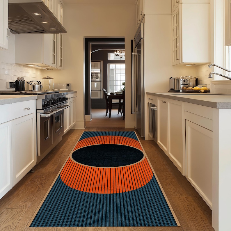 May include: A rectangular kitchen rug with a geometric design. The rug features a large black oval in the center, surrounded by a vibrant orange semi-circle and blue vertical stripes. The rug is placed on a wooden floor.