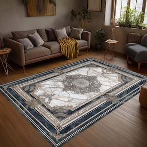May include: A rectangular area rug with a marble-like design. The rug features a white and gray center with a dark blue border and ornate, gold-colored accents. The rug is placed on a wooden floor in a living room setting.