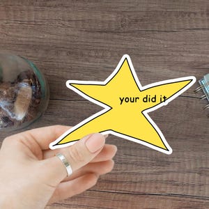 Könnte beinhalten: Ein gelber Stern-Aufkleber mit dem Text "your did it" auf einer Holzoberfläche.