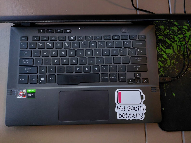May include: A black laptop with a sticker that says "My social battery" and a low battery icon. The laptop has a black keyboard and a touchpad.