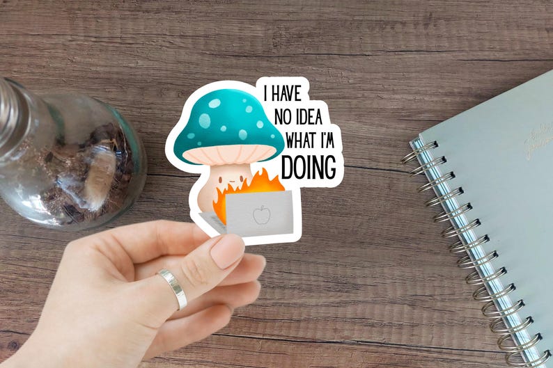 May include: A sticker featuring a cartoon mushroom with a teal cap and white spots, holding a burning laptop. The text "I HAVE NO IDEA WHAT I'M DOING" is displayed in black. The sticker is held by a hand.