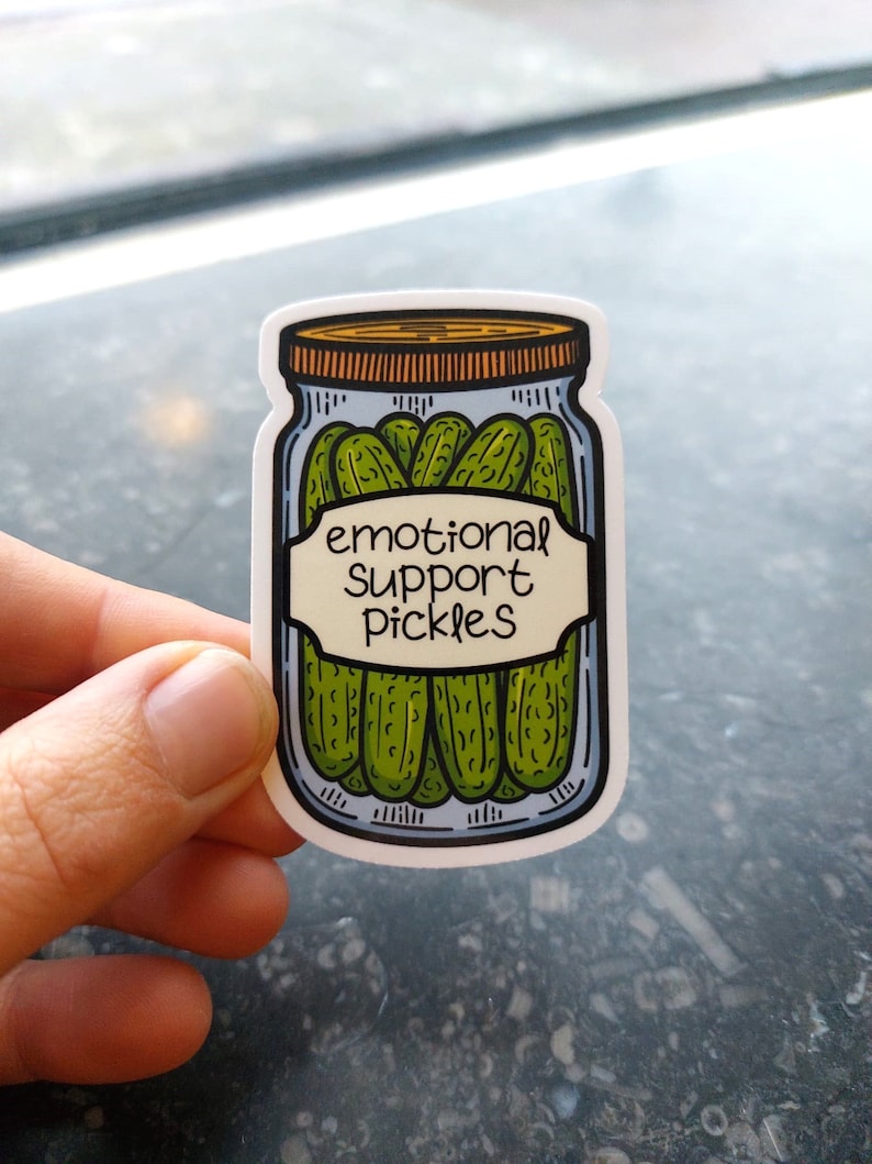 May include: A white sticker with a cartoon drawing of a jar of pickles. The jar has a brown lid and a white label that says "emotional support pickles".