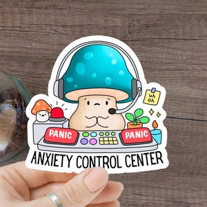 Op de afbeelding: Een sticker met een cartoon-paddenstoel die een headset draagt en aan een bedieningspaneel zit met knoppen met het label "Paniek". De tekst "Angst Controle Centrum" staat onder het paneel.