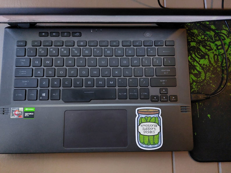 May include: A sticker on a laptop computer with a drawing of a jar of pickles. The jar has a label that reads "Emotional Support Pickles".