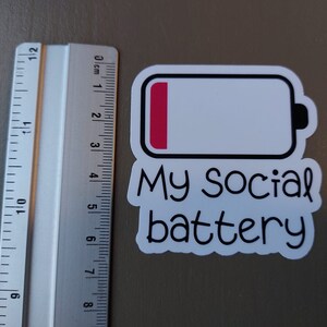 May include: A white sticker with a black outline of a battery icon. The battery is almost empty, with only a small red bar at the top. The text "My Social battery" is written below the battery icon.