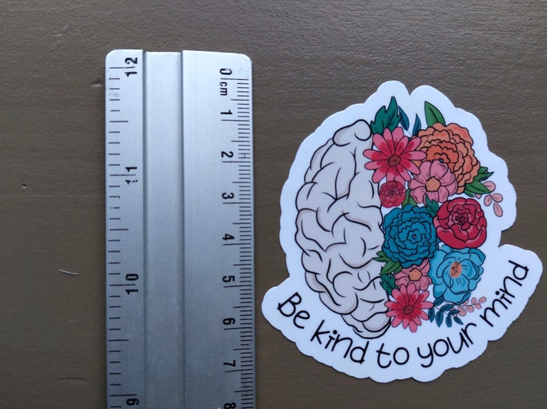 May include: A white sticker with a gray brain outline and colorful flowers. The text "Be kind to your mind" is written in a white cursive font.