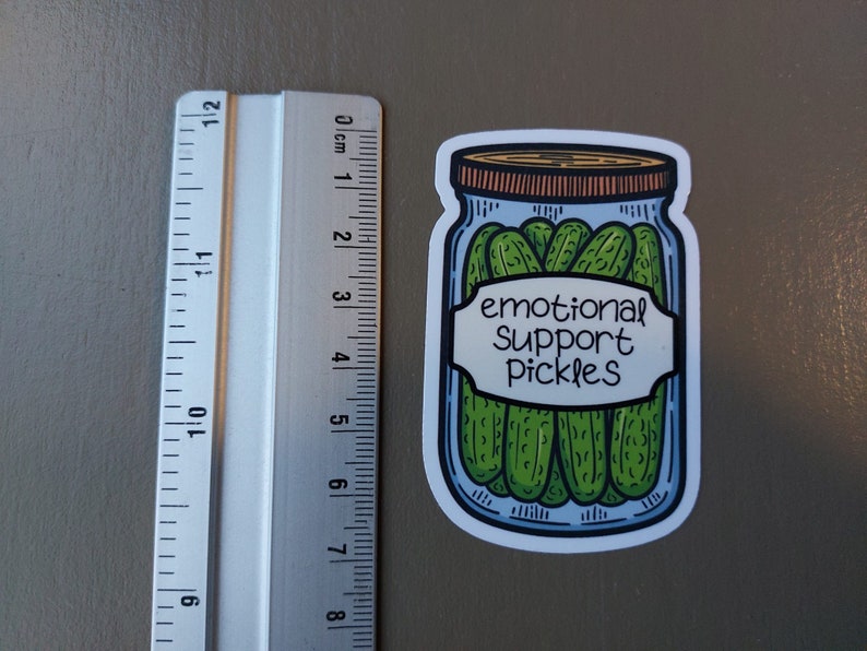 May include: A white sticker with a cartoon illustration of a glass jar filled with green pickles. The jar has a brown lid and a white label that reads "emotional support pickles".